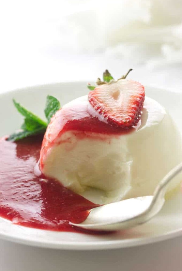 Panna cotta serving with spoon and bite, puddle of strawberry sauce