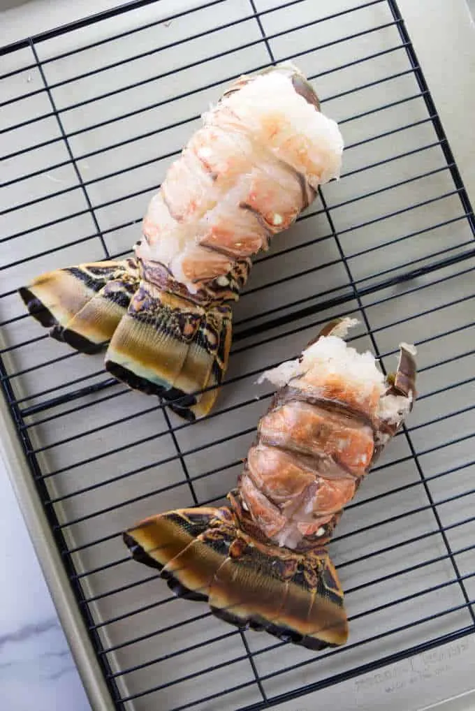 Two raw lobster tails ready to be broiled.