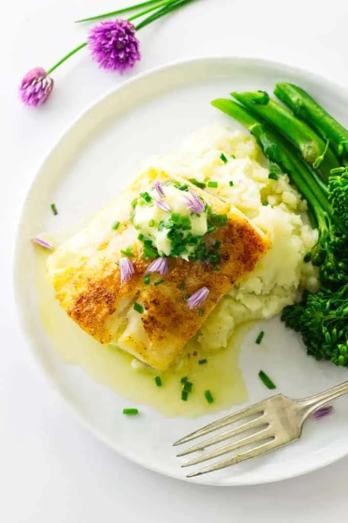 overhead view of broiled cod with chive butter garnished with chives and bits of a chive blossom mashed potatoes and broccolini,
