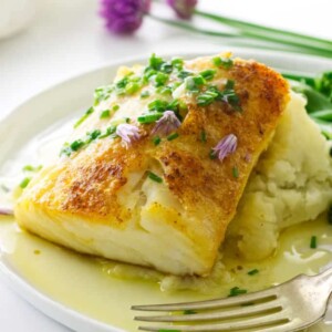 close up view of plated Fillet of cod on mashed potatoes, chive blossoms and napkins in background