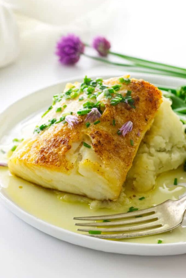 close up view of plated Fillet of cod on mashed potatoes, chive blossoms and napkins in background