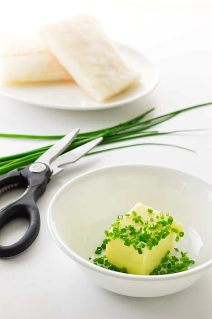Dish with butter and snipped chives, cod fillets, scissors, chives in the background