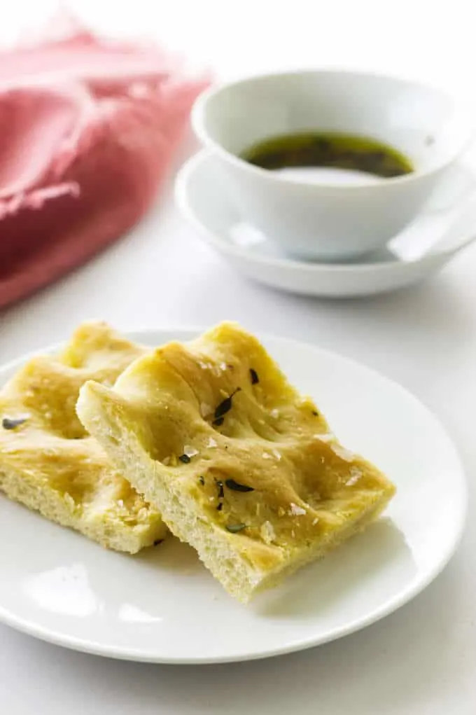 two pieces of focaccia bread on a saucer, a small dish of garlig-herb-oil in the background with pink napkin