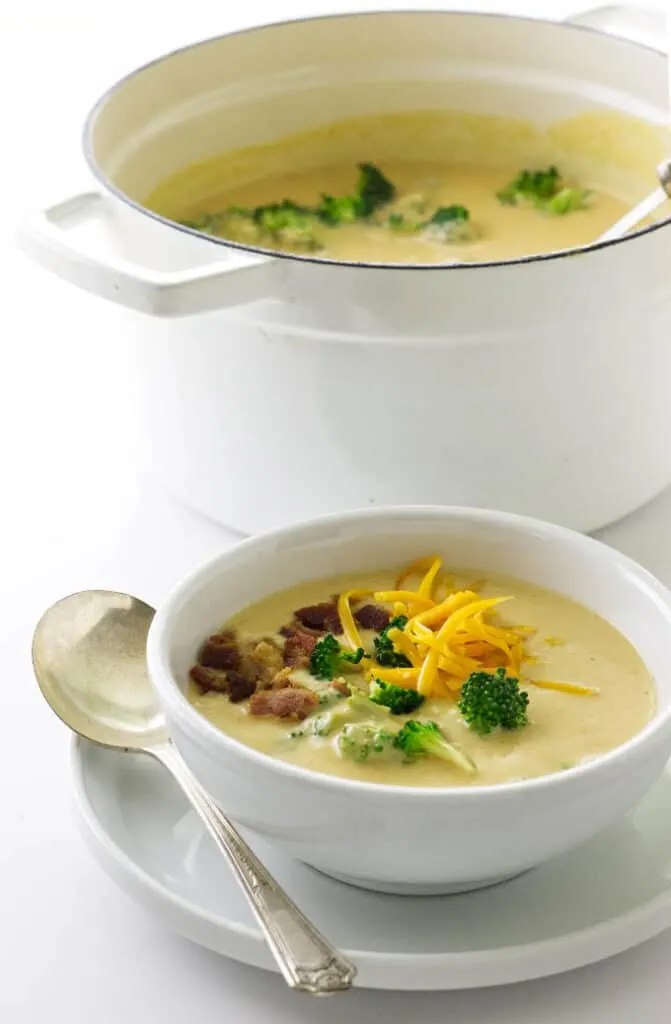 Pot of soup with ladle, bowl of soup garnished with bacon, cheddar and broccoli