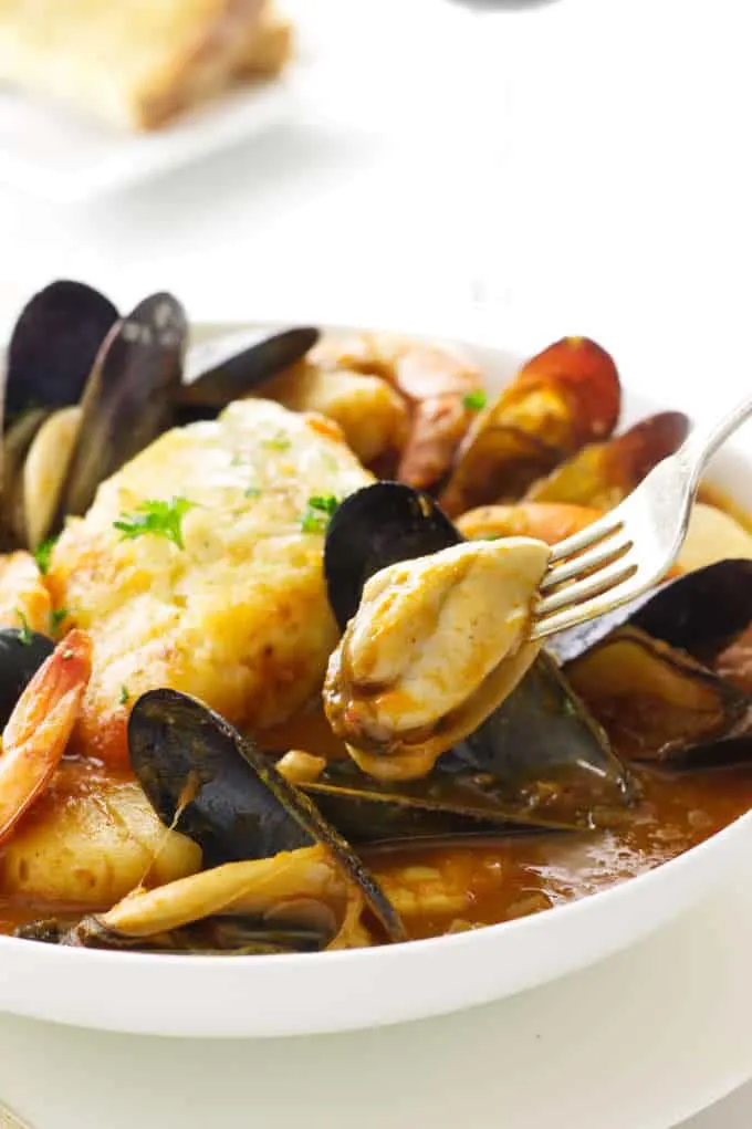 Serving of seafood in romesco sauce with a mussel on a fork