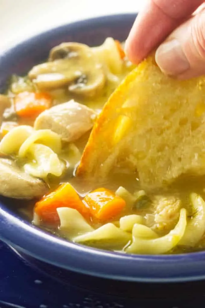 close up view of turkey noodle soup with bread dipped into soup