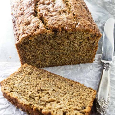 A freshly baked loaf of spelt banana bread with a knife at the side.