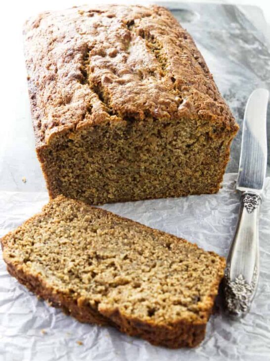 A freshly baked loaf of spelt banana bread with a knife at the side.