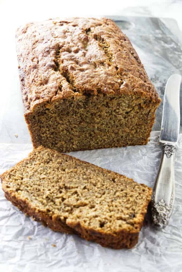 A freshly baked loaf of spelt banana bread with a knife at the side.