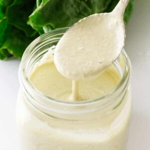 Jar of Caesar Salad Dressing with a spoonful, romaine lettuce in background