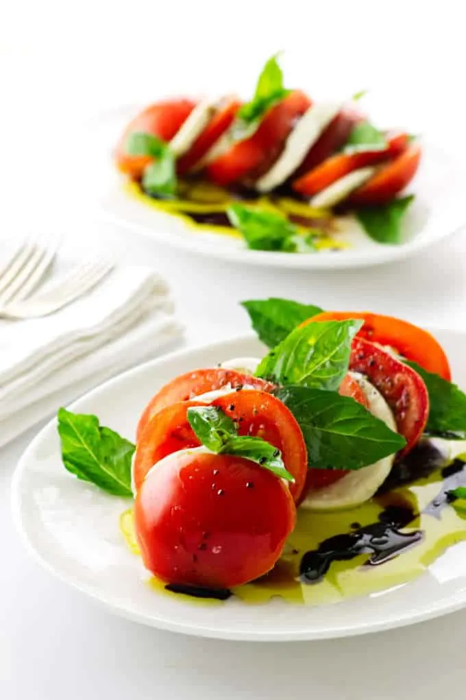 Photo of two servings of tomato, mozzarella and basil salad with oil/vinegar dressing