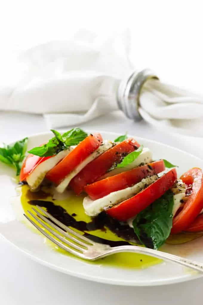 Caprese salad on a plate with fork, napkin in backround