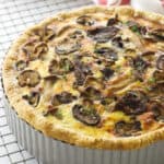 Overhead view of mushroom and goat cheese quiche on cooling rack, towel in background