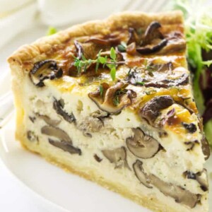 Close up view of a slice of quiche on a plate with a fork, napkin in the background