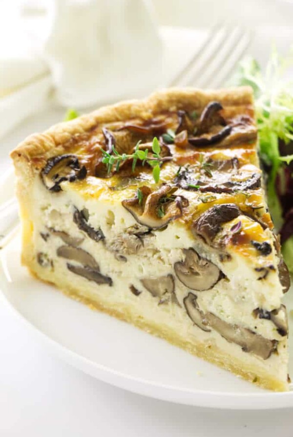 Close up view of a slice of quiche on a plate with a fork, napkin in the background