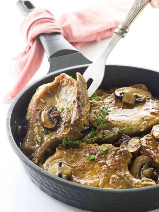 Pork chops and mushrooms in skillet with serving fork