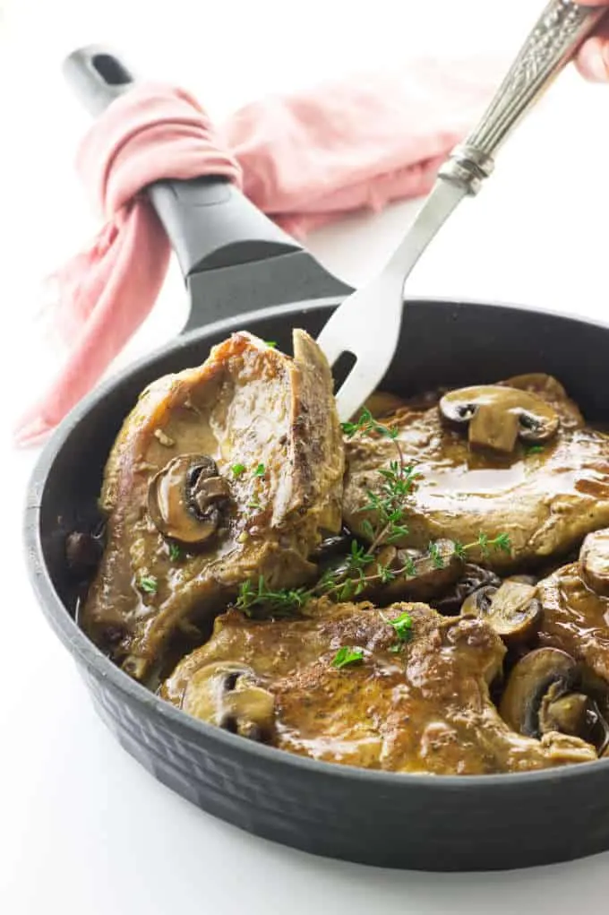 Pork chops and mushrooms in skillet with serving fork