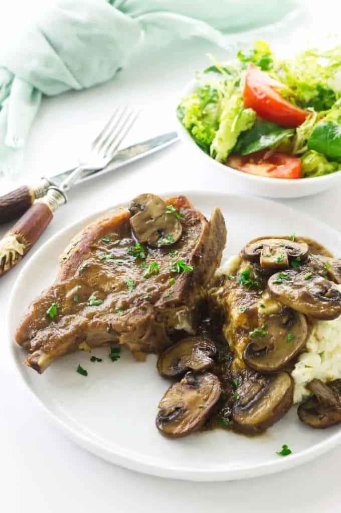 Overhead view of pork chop, mushrooms, mashed potatoes. Salad, fork/knife and napkin