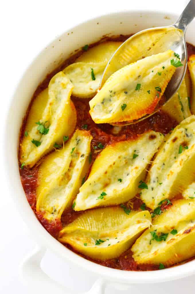 Dish with baked pasta shells and one stuffed shell in a spoon
