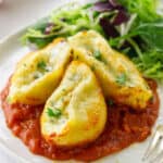 Close up of 3 stuffed pasta shells on marinara sauce and side salad