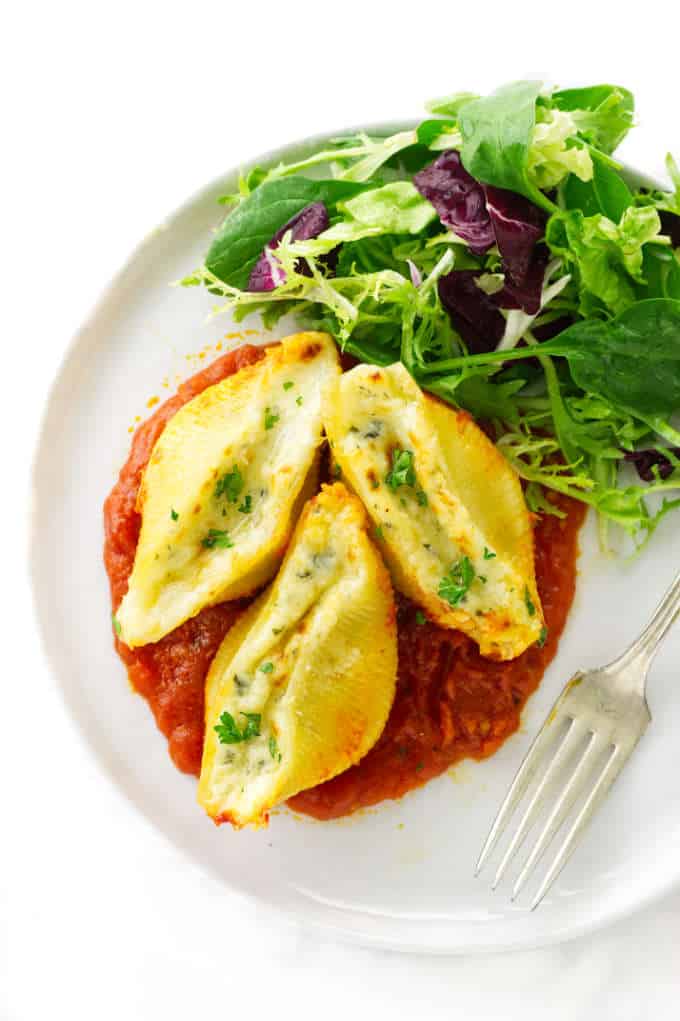 Overhead view of a serving of stuffed pasta shells, marinara sauce, salad and a fork