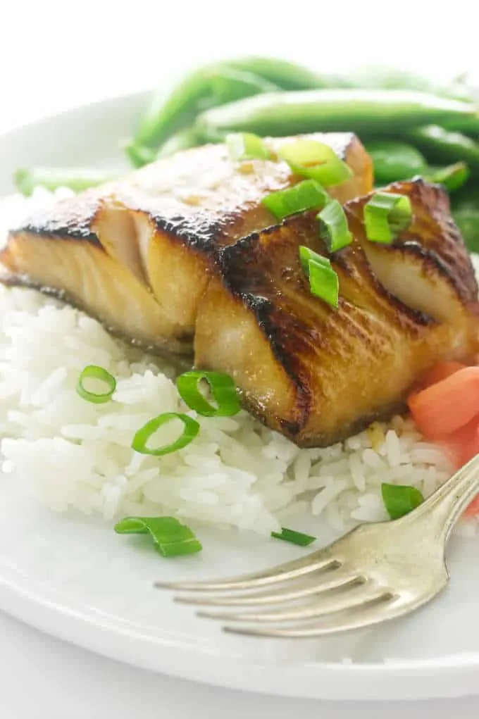 serving of fish with onion garnish on rice with fork, pickled ginger and snap peas