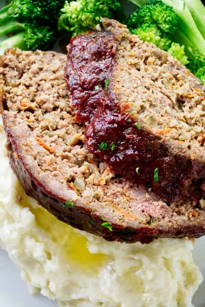 Two slices of pork and beef meatloaf on a pile of mashed potatoes.