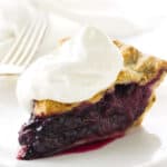 slice of pie topped with whip cream, fork and napkin in background