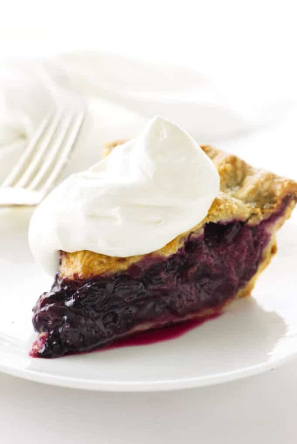 slice of pie topped with whip cream, fork and napkin in background