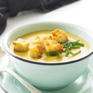 Bowl of soup, homemade crouton, chopped sage and a spoon. Black napkin in background