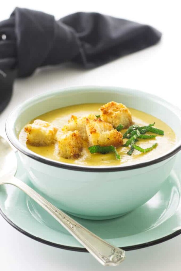 Bowl of soup, homemade crouton, chopped sage and a spoon. Black napkin in background