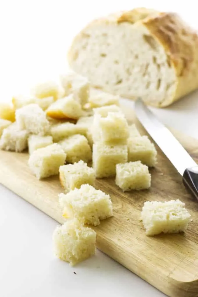 Sourdough bread cut into cubes on cutting board with knife