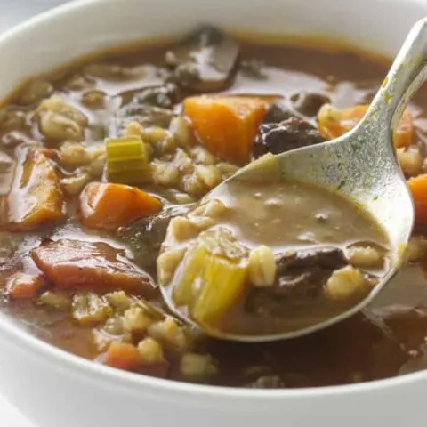 A spoon in a bowl of beef barley soup.