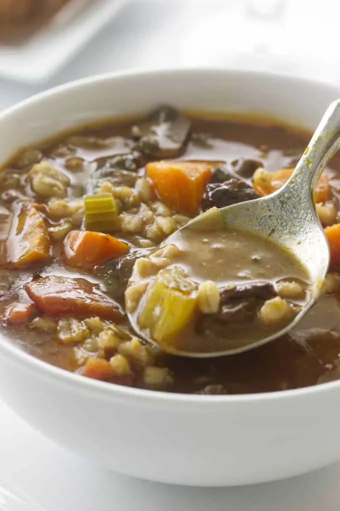 A spoon in a bowl of beef barley soup.