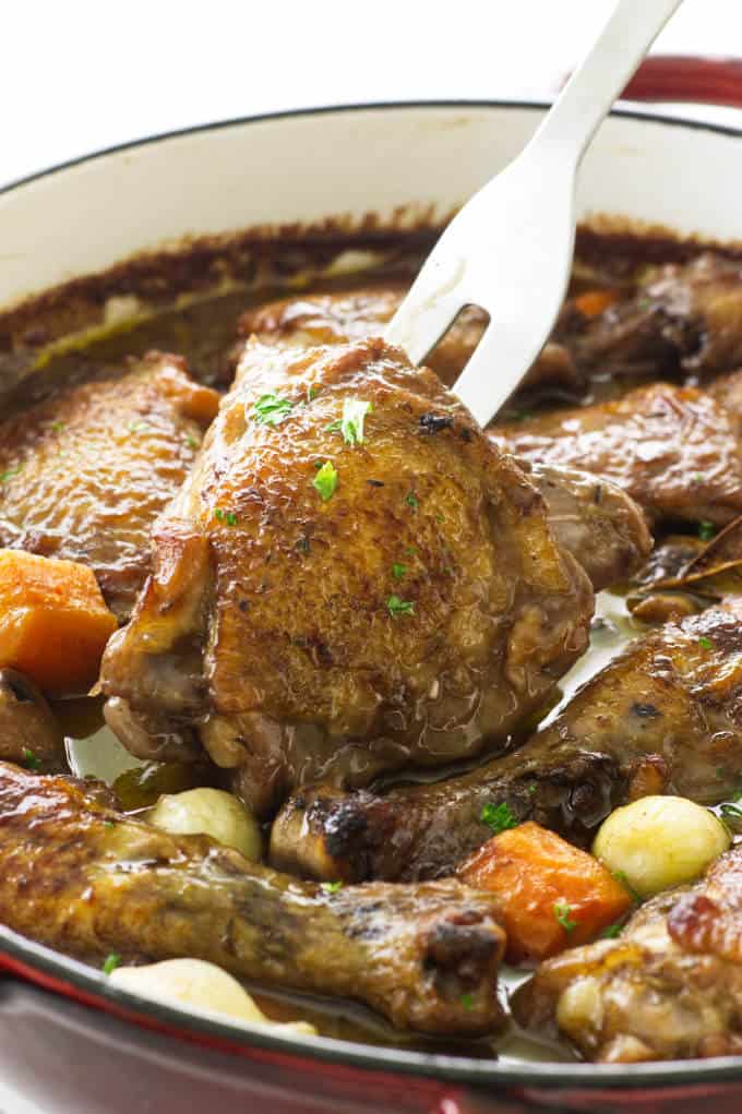 Close up view of baked coq au vin with a fork lifting a serving of chicken