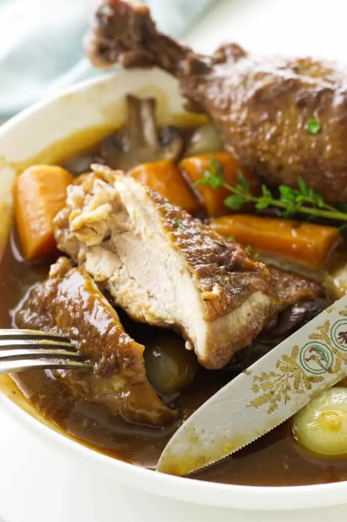 close up view of a serving of coq au vin and a knife/fork cutting chicken
