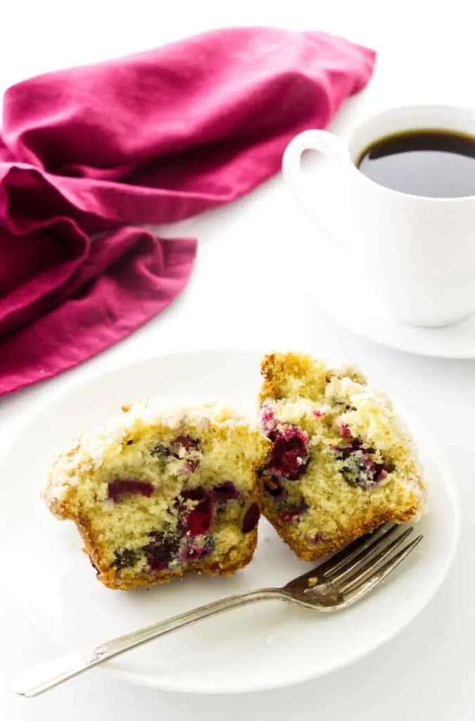 Overhead view of a cranberry muffin on a serving plate with a fork. Napkin and coffee in background