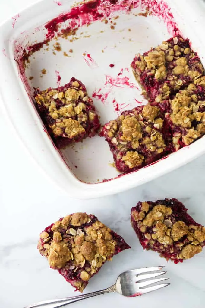 Four raspberry bars in a baking dish and two on the counter.