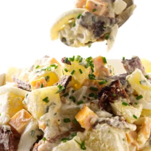 A spoon scooping a serving of potato salad with bacon and eggs.