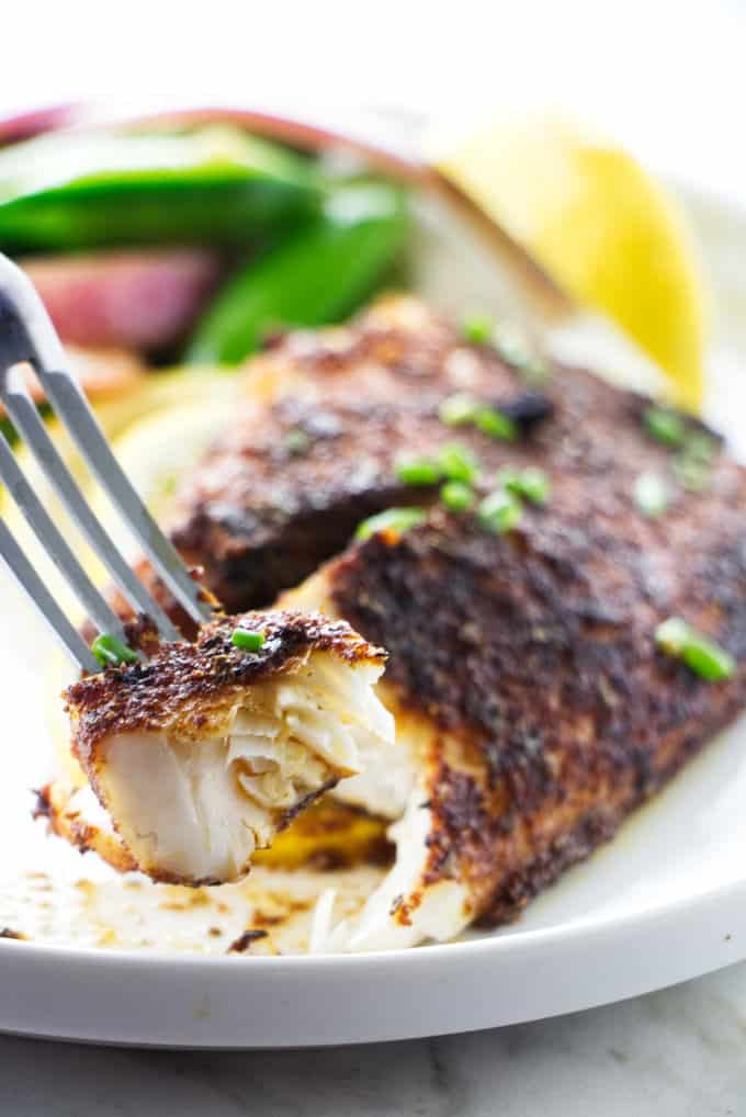 A bite of blackened tilapia on a fork.