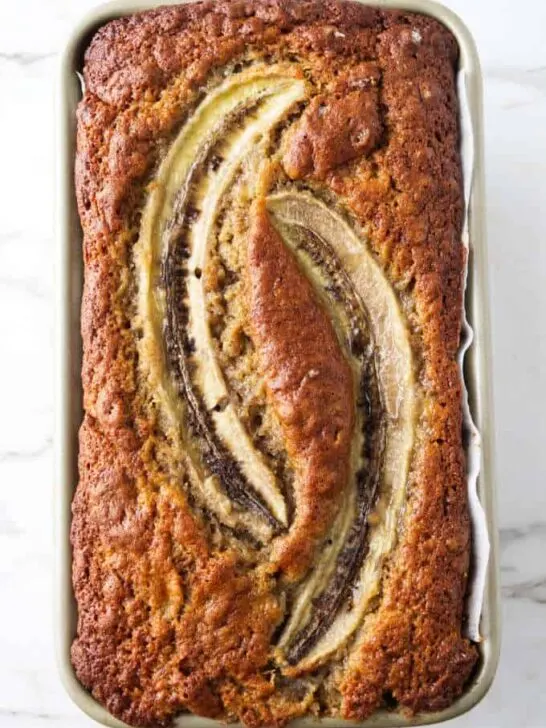 Sourdough banana bread baked in a loaf pan with two halves of bananas on top.