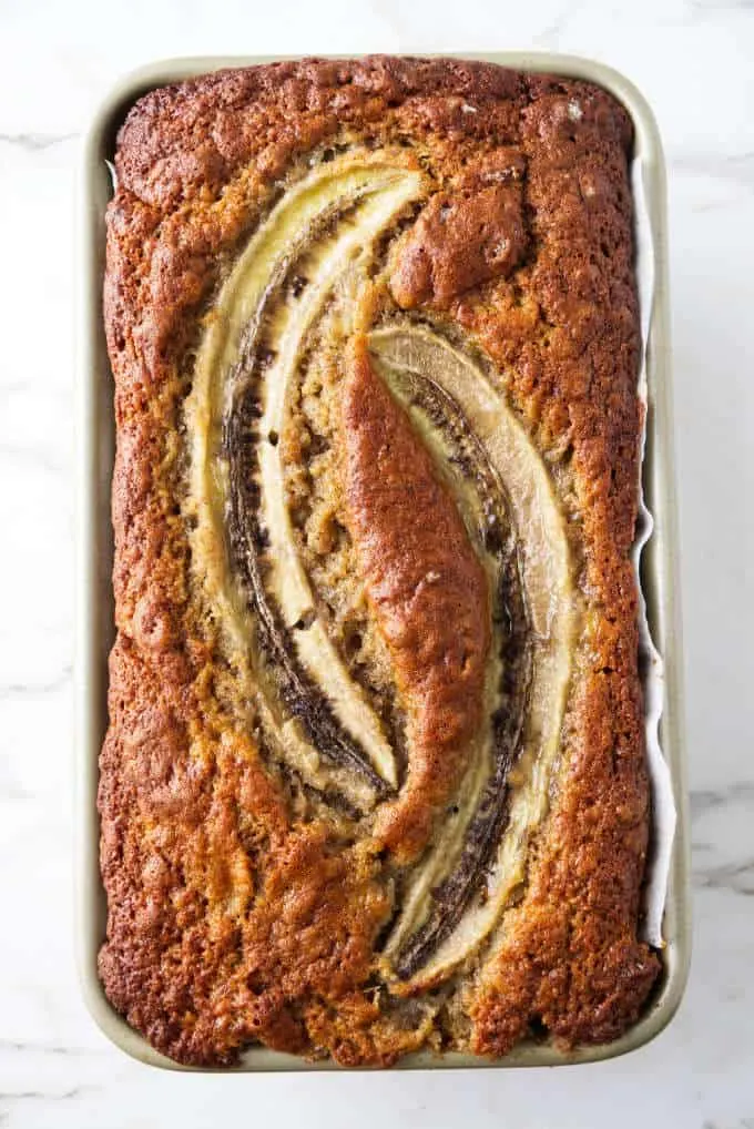 Sourdough banana bread baked in a loaf pan with two halves of bananas on top.