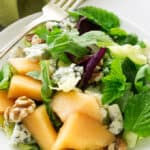 A serving of cantaloupe blue cheese salad with fresh mint leaves.