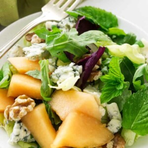 A serving of cantaloupe blue cheese salad with fresh mint leaves.