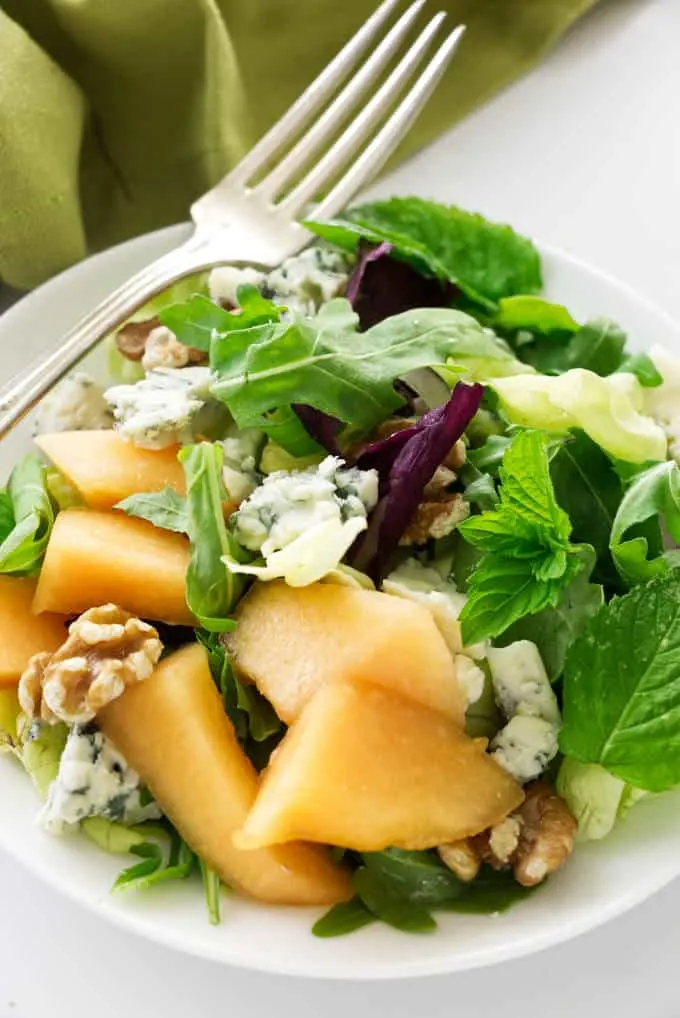 A serving of cantaloupe blue cheese salad with fresh mint leaves.