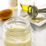 close view of a jar of salad dressing, 1/2 orange, stick blender and ingredients in background