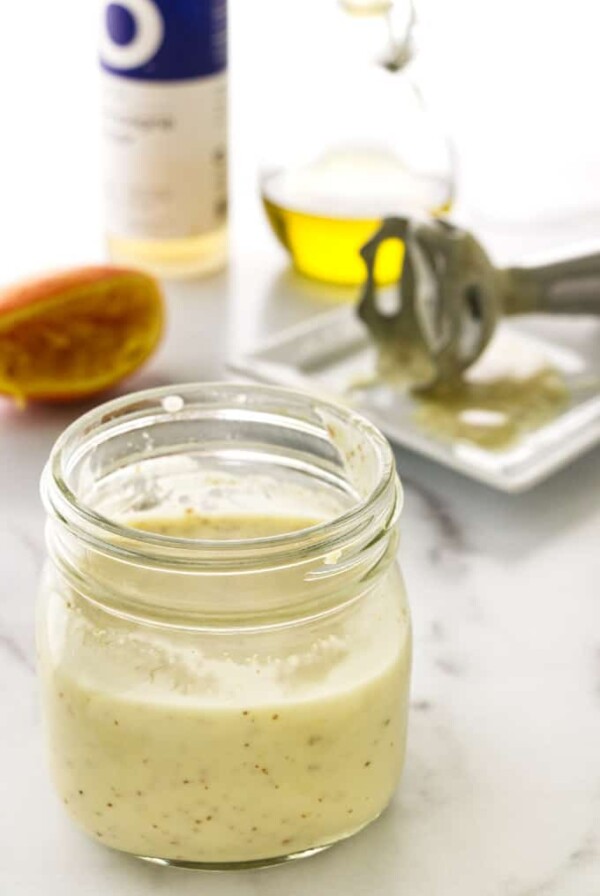 close view of a jar of salad dressing, 1/2 orange, stick blender and ingredients in background