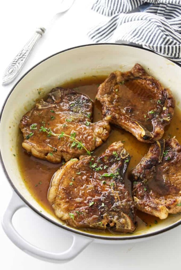 Four pork chops in a skillet with honey garlic glaze.