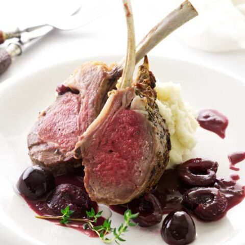 Lamb with red wine cherry sauce on a plate with mashed potatoes.