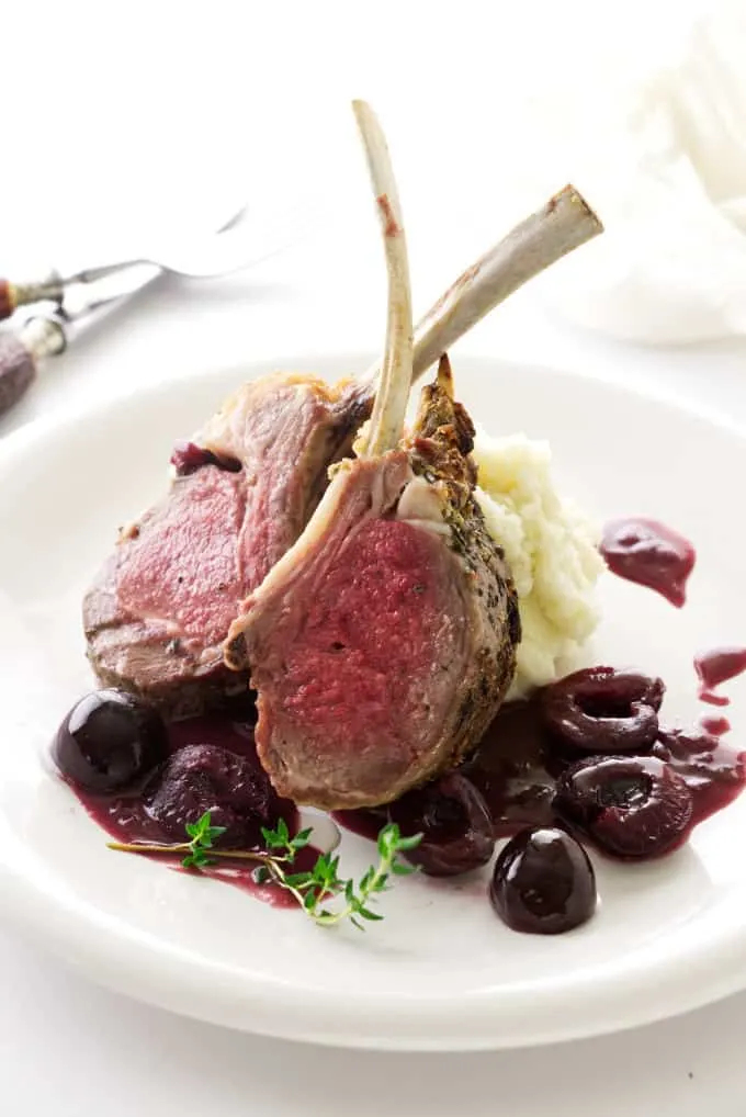 Lamb with red wine cherry sauce on a plate with mashed potatoes.